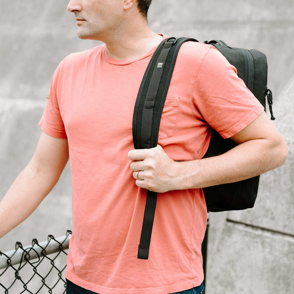 Man wearing black 21L cordura backpack over one shoulder showing the Scioto Made embroidered bars on the strap 