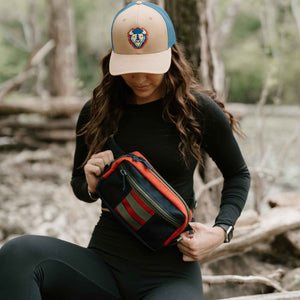 Women holding Lane Sling Bag while out on a hike.  Lane sling bag is navy and red 1000D Cordura with Olive straps and attachment loops.