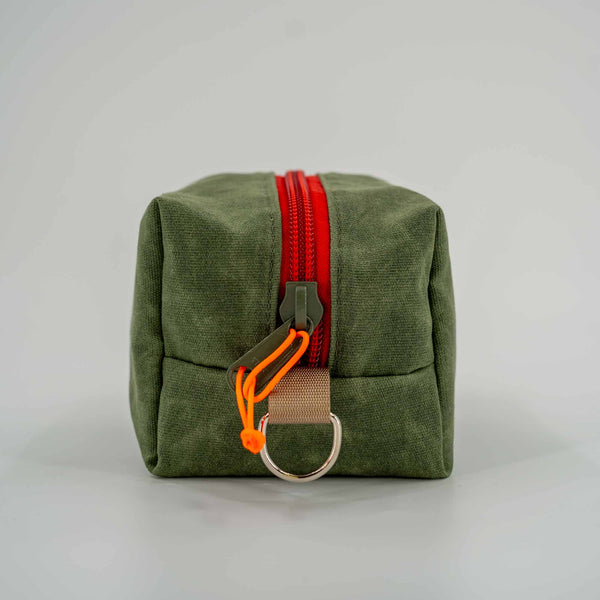 Side view of green waxed canvas Travel Dopp Kit: Sleek profile with metal D-ring for attachment and YKK #10 zipper.