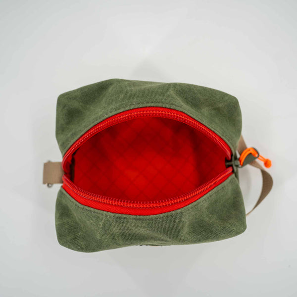 Inside view of green waxed canvas Travel Dopp Kit: Roomy main compartment for essentials, easy-to-clean eco XPack liner in bright orange, and YKK #10 zipper in red.