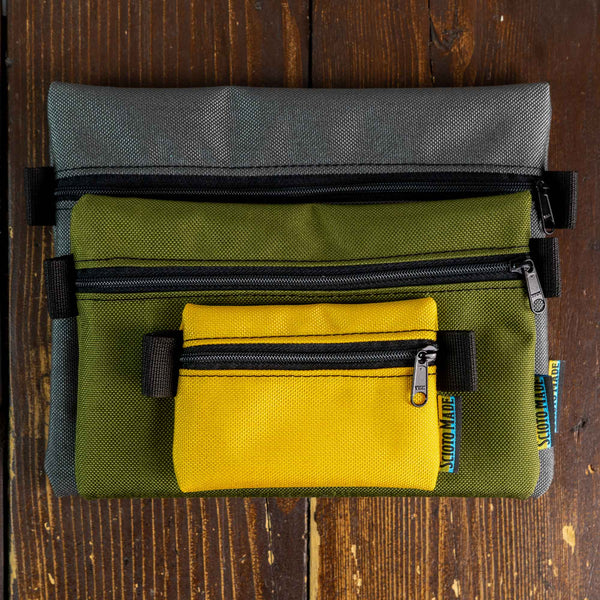 Image showing three accessory bags in yellow, olive, and smoke colors. Sizes include Mini (4.5" x 3.5"), Small (8.25" x 5.75"), and Medium (9" x 7.75"). Made from durable 1000D Cordura fabric with a 400D pack cloth interior. Perfect for organizing everyday carry items or travel essentials. Made in USA.
