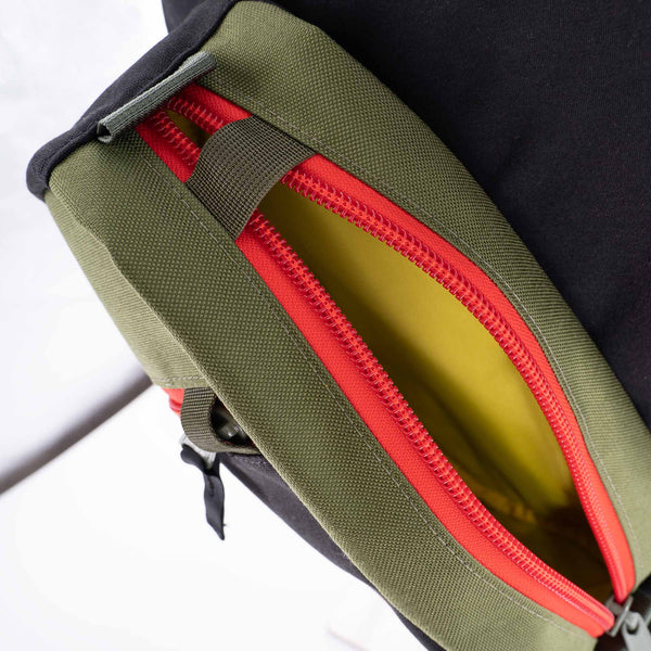 The Hayden urban sling bag in black and olive with red zipper. Yellow inside.