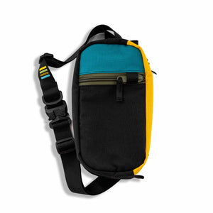The Hayden sling bag is ready to go on any adventure!  This urban sling bag is made for everyday travel and hiking. Made with 1000D Cordura, it’s rugged enough to take on your hiking adventures and light enough for a trip to your favorite outdoor patio. Front view with exterior colors of black, teal, yellow and features an olive-green zipper.