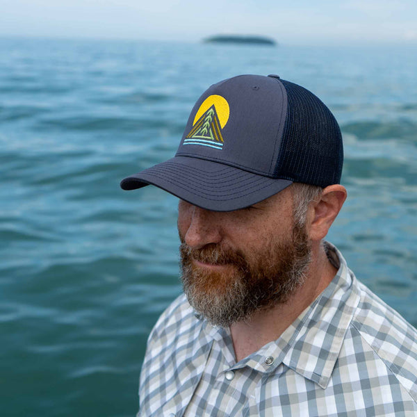 Man wearing a classic structured 5 panel navy trucker hat with pre-curved bill and adjustable snapback closure embordered with tree design on front 